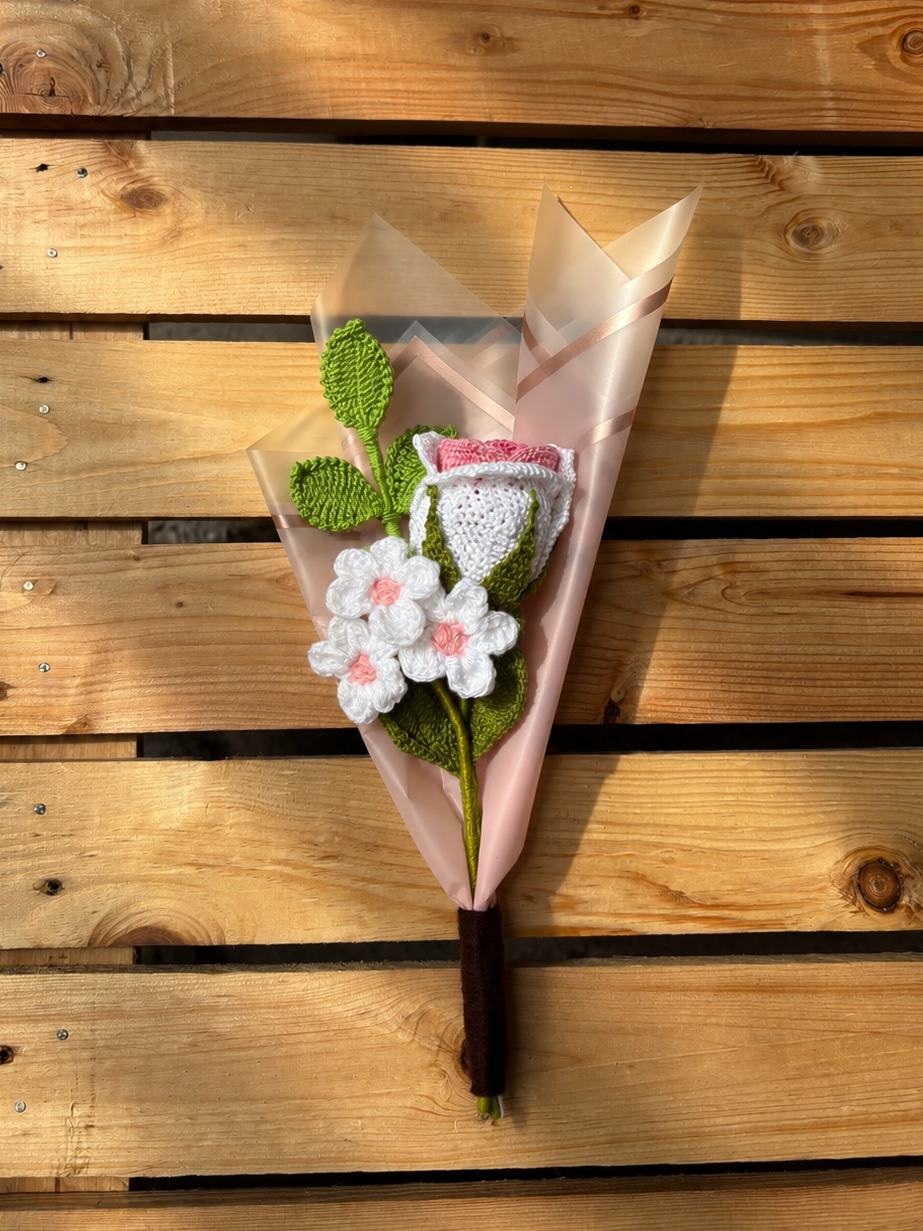 Bouquet of crocheted flowers in pink paper on a wooden surface